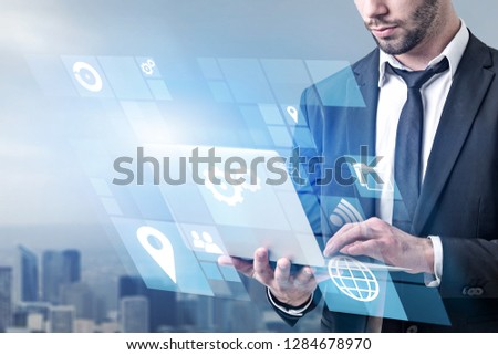 Unrecognizable businessman holding laptop with business interface icons standing over blurred cityscape background. Toned image double exposure