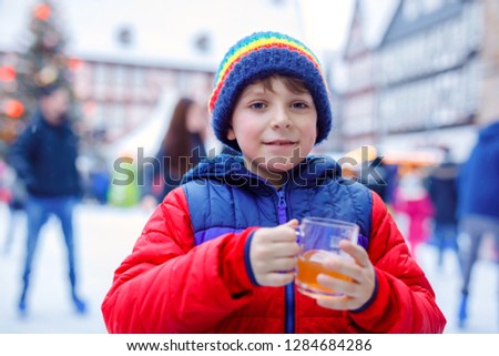 Happy little kid boy in colorful warm clothes on skating rink of Christmas market or fair drinking hot punch or chocolate. Healthy child having fun on ice skate. people having active winter leisure