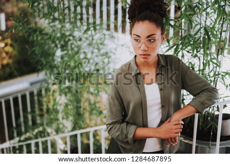 Waist up portrait of attractive young lady in glasses looking away with serious expression while leaning on handrail. Copy space in left side