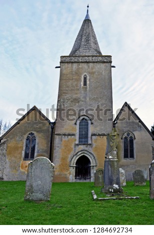 The front view of a Church in Kent England, the church has a pointed steeple, stained glass windows and a large wooden door and is situated in the graveyard with blue sky background.