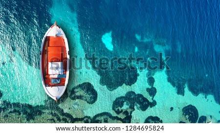 Aerial drone top view photo of traditional red fishing boat anchored in exotic mediterranean destination with turquoise and emerald sea