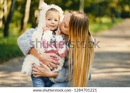 young blonde mother kneeling and hugginb the girl toddler in the park on a sunny day