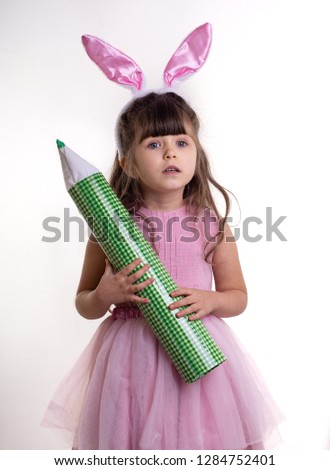 Little girl dressed as the Easter bunny standing on white background and holding pencil. Child Easter Holiday Concept. Isolated. Good for advertising text. 