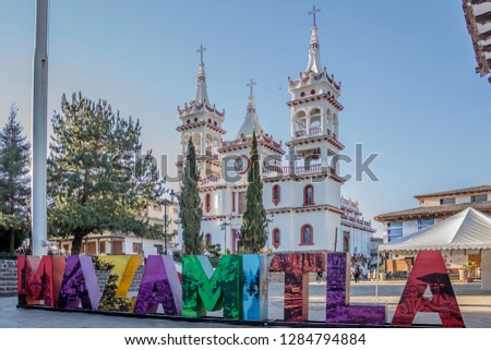 Low angle view of Church of San Cristóbal against blue sky, eclectic style with its white walls and small detanes in red with the word Mazamitla in front, sunny day in Jalisco, Mexico Royalty-Free Stock Photo #1284794884