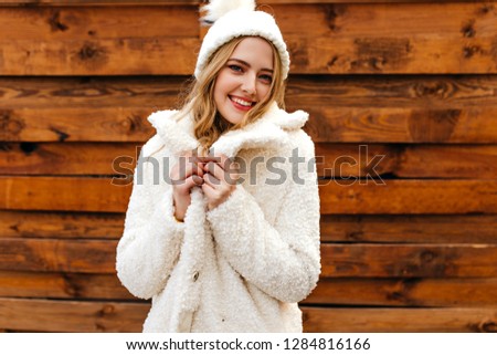 The girl in eco fur coat smiles and looks into the camera. Photo of the blonde in winter