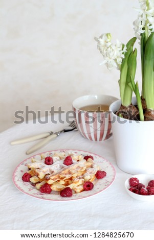 Breakfast table with fresh waffles and raspberries on the table