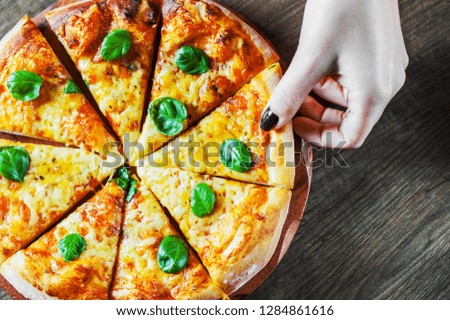 woman Hand takes a slice of Pizza with Mozzarella cheese, Tomatoes, pepper, Spices and Fresh Basil. Italian pizza. Pizza Margherita or Margarita on wooden table background