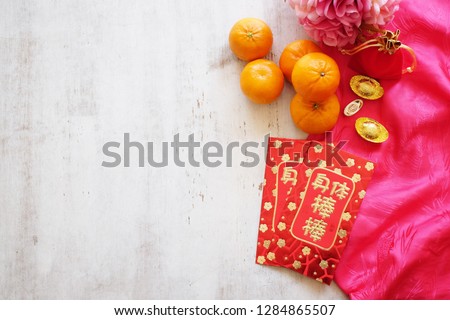 Chinese New Year festival concept. Mandarin oranges, red envelopes, red pocket and gold ingots on red silk with old wooden background. Chinese characters mean rich, wealthy, healthy and happy