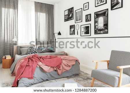 Armchair next to bed with pink blanket in modern bright bedroom interior with gallery. Real photo