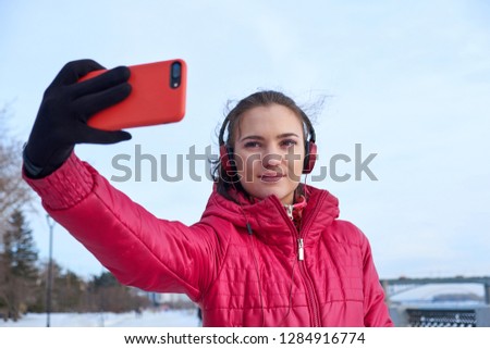 Young girl with headphones and jacket take selfie from hands with phone on winter