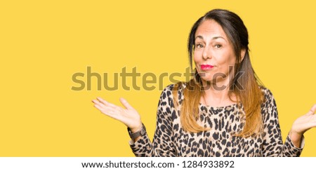 Beautiful middle age woman wearing leopard animal print dress clueless and confused expression with arms and hands raised. Doubt concept.