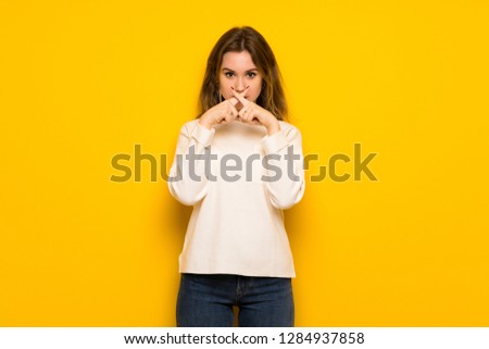 Teenager girl over yellow wall showing a sign of silence gesture