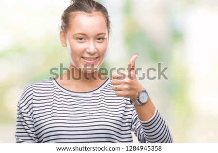 Young beautiful caucasian woman over isolated background doing happy thumbs up gesture with hand. Approving expression looking at the camera with showing success.