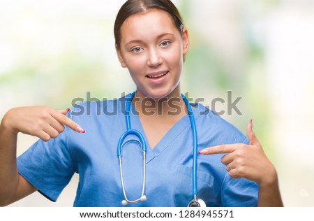 Young caucasian doctor woman wearing medical uniform over isolated background looking confident with smile on face, pointing oneself with fingers proud and happy.