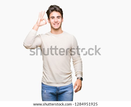 Young handsome man over isolated background smiling positive doing ok sign with hand and fingers. Successful expression.
