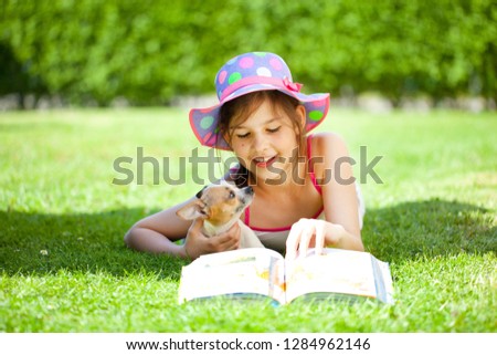 A girl reading book with little puppy in garden