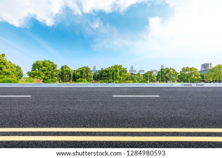Urban asphalt road and green trees under blue sky