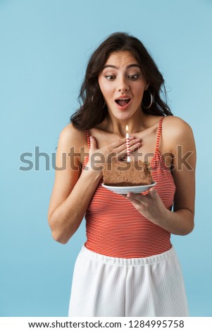 Lovely cheerful girl wearing summer clothes standing isolated over blue background, eating birthday cake