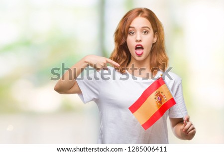 Young beautiful woman holding flag of spain over isolated background with surprise face pointing finger to himself