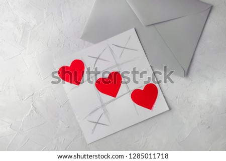 Valentine day handmade greetings card - tic tac toe game with hearts, grey envelope, white concrete background