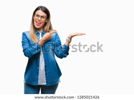 Young beautiful woman over wearing glasses over isolated background amazed and smiling to the camera while presenting with hand and pointing with finger.