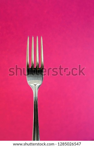 Shiny metal fork. Kitchen appliance. The view from the top. Close photo. High resolution. Violet (pink) background.