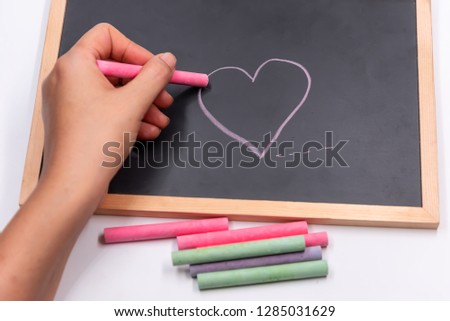 Hand hold color chalk draw cartoon heart shape on blackbroad.Tell love in valentine day or tell save good health and heart.