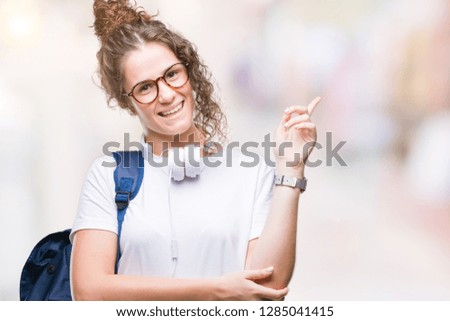 Young brunette student girl wearing backpack and headphones over isolated background with a big smile on face, pointing with hand and finger to the side looking at the camera.