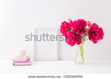 Mockup with a white frame and red peonies in a vase on a light background