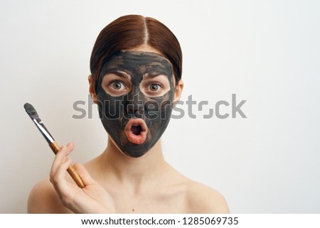 surprised woman in a clay mask in hand brush