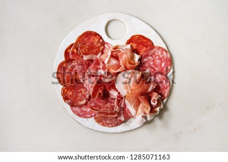Antipasto meat platter assorti of sliced jamon, salami, chorizo sausage on white ceramic board over white marble background. Flat lay, copy space Royalty-Free Stock Photo #1285071163
