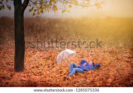 girl in a park with an umbrella lies on the autumn leaves and rests enjoying nature