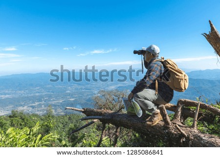 Young man with backpack and holding a binoculars and map sitting on top of mountain.