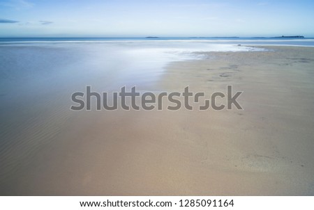 A tranquil scene of the beach at Bamburgh, Northumberland, with sand and a stream flowing towards the sea.
