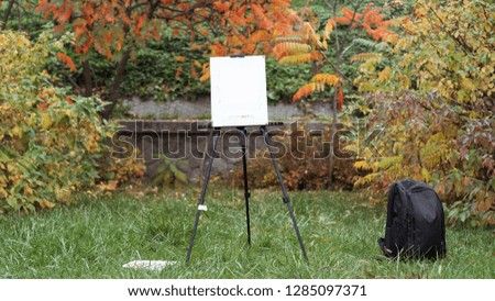 Easel, black backpack and paints are standing on the grass in the autumn park. Autumn concept