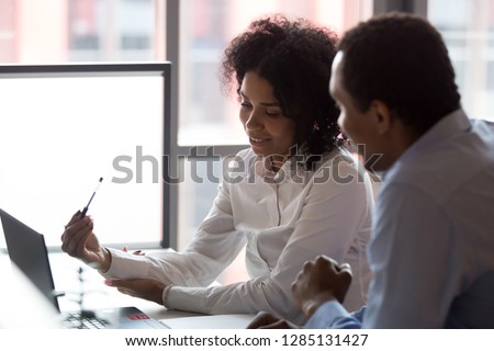 Mixed race pretty millennial businesswoman sitting together with african american business partner, smart people negotiating using computer looking at device screen cogitating making decision concept Royalty-Free Stock Photo #1285131427