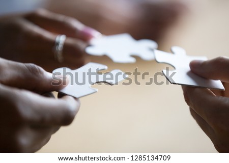 Close up hands of african american and caucasian associates multinational teammates holding white pieces of puzzle, people searching and finding solution. Team building, teamwork and support concept