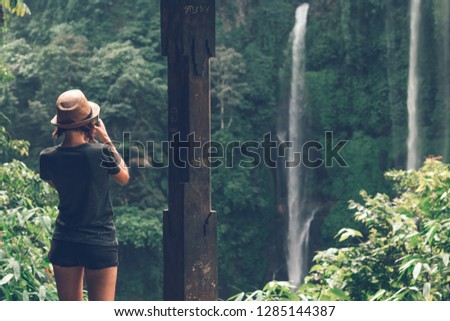 Young woman tourist taking photo of the Sekumpul waterfall, magic island of Bali, Indonesia.