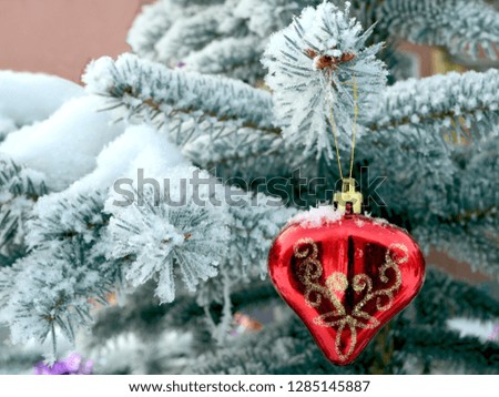 Christmas background: toy red heart on snow-covered pine branches in the street