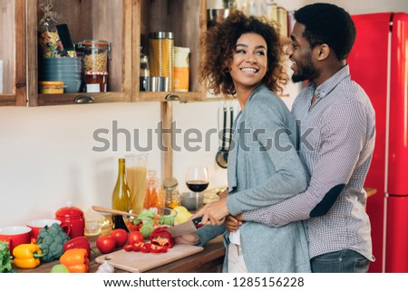 Amorous black couple cooking together in kitchen, loving husband embracing his cooking wife, copy space