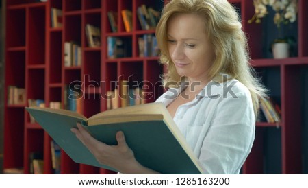 young woman reading a book in the library on the background of bookshelves