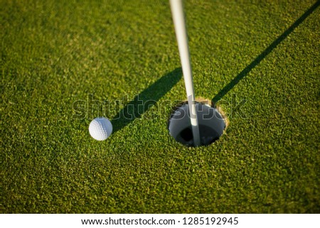 Single golf ball sitting near a hole on a golf course.
