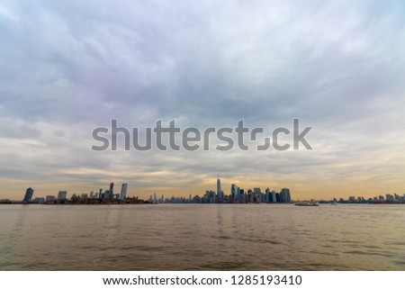 View of New York City skyline with dramatic sky at dusk from Liberty Island, New York, USA