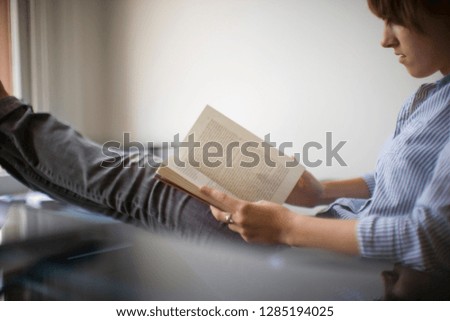 Young woman sitting reading a book with her legs stretched out.