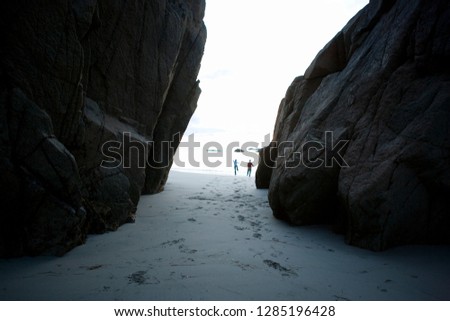 Running through a gap in some big rocks on a beach.