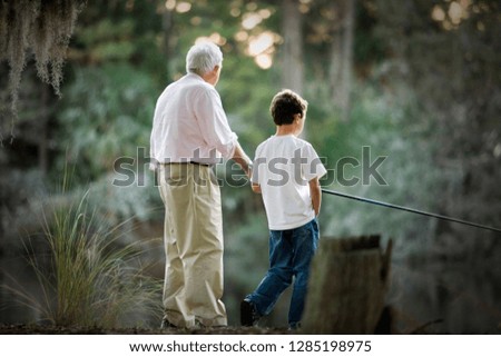 Senior adult man fishing in a lake with his young grandson.