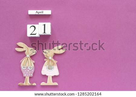 Wooden cubes calendar April 21 and pair of wooden easter bunnies on purple paper background. Concept Catholic Easter Copy space Template for lettering, text or your design Creative Top View.