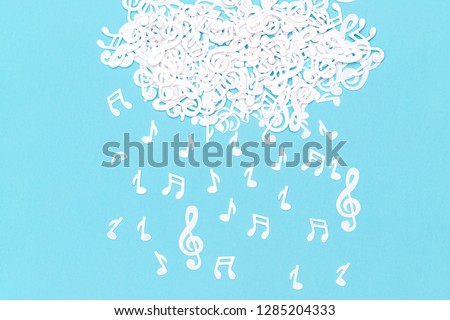 Musical confetti cloud and rain on blue background, close up. Musical symbols creative minimalistic background, flat lay. Falling Musical Notes as rain.