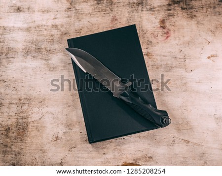 big grey knife lying on blank black closed book on wooden table. Top view