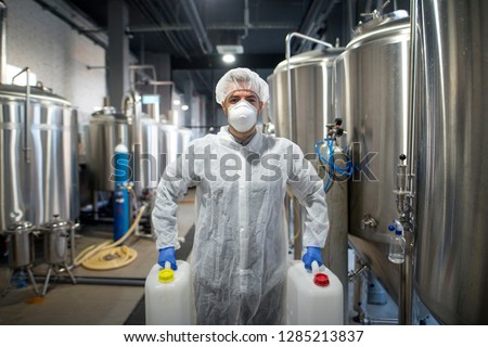 Industrial worker holding plastic cans with chemicals in production plant. Technologist wearing protection white uniform handling with aggressive chemicals substances. Royalty-Free Stock Photo #1285213837